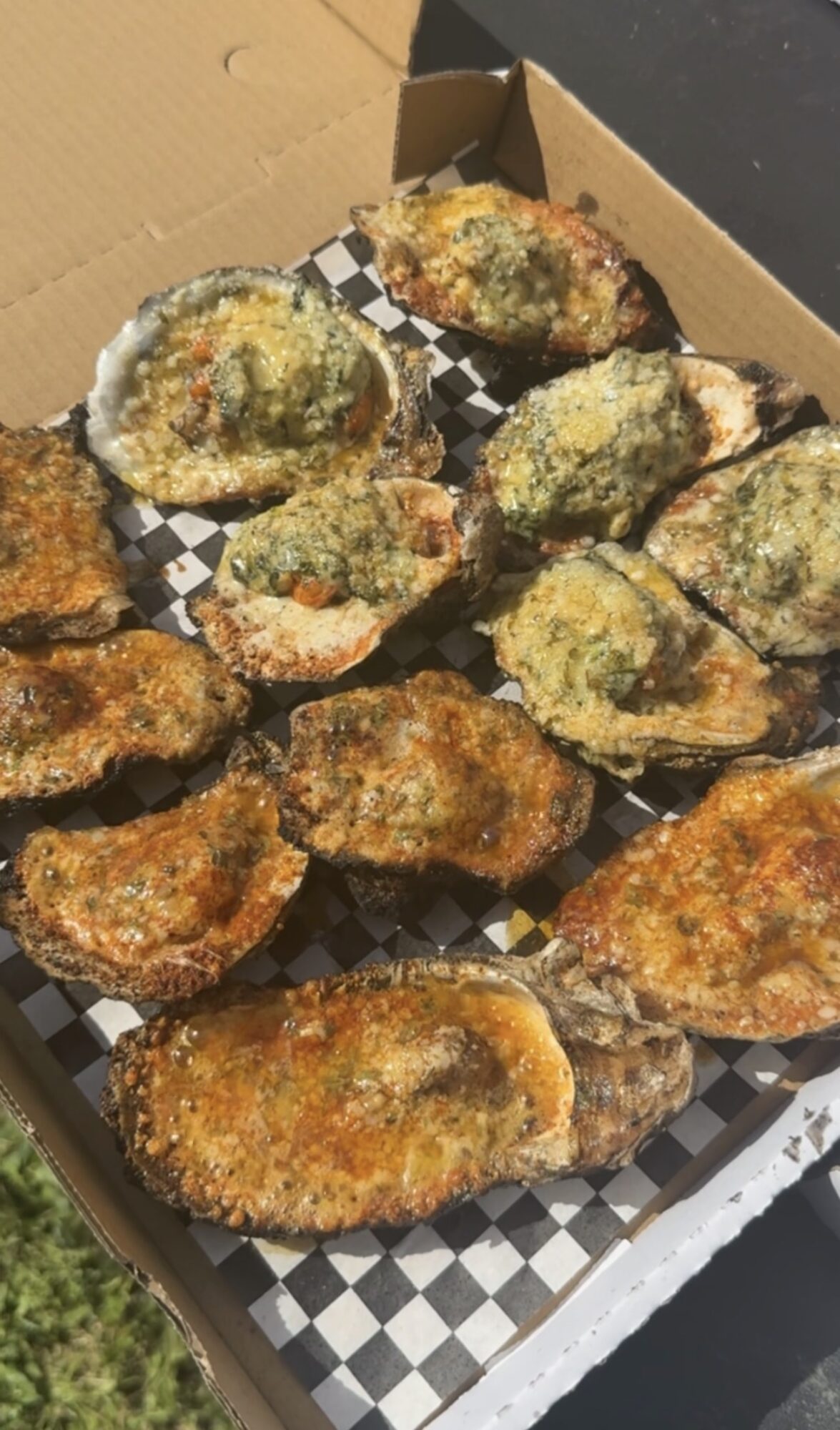 Fried oysters in a box with black and white checkered paper, some with green herbs, some with breading, on a black surface