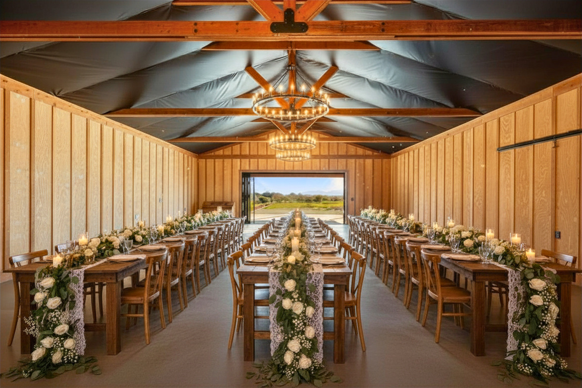 Long banquet table decorated with flowers and candles inside a wooden-paneled room with a view outside, chandelier overhead.