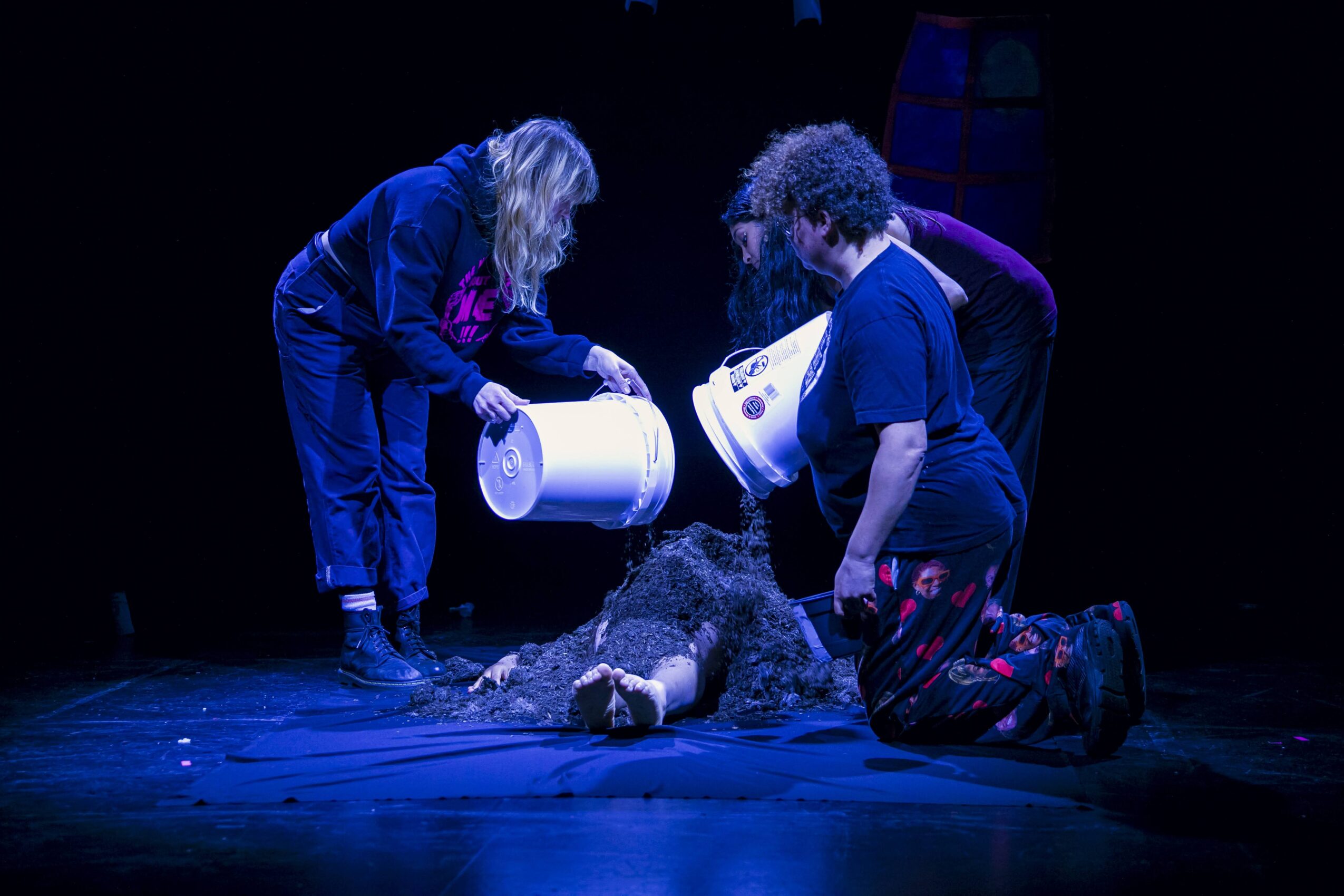 Three people pour water on a dog lying on the floor in a dark setting.