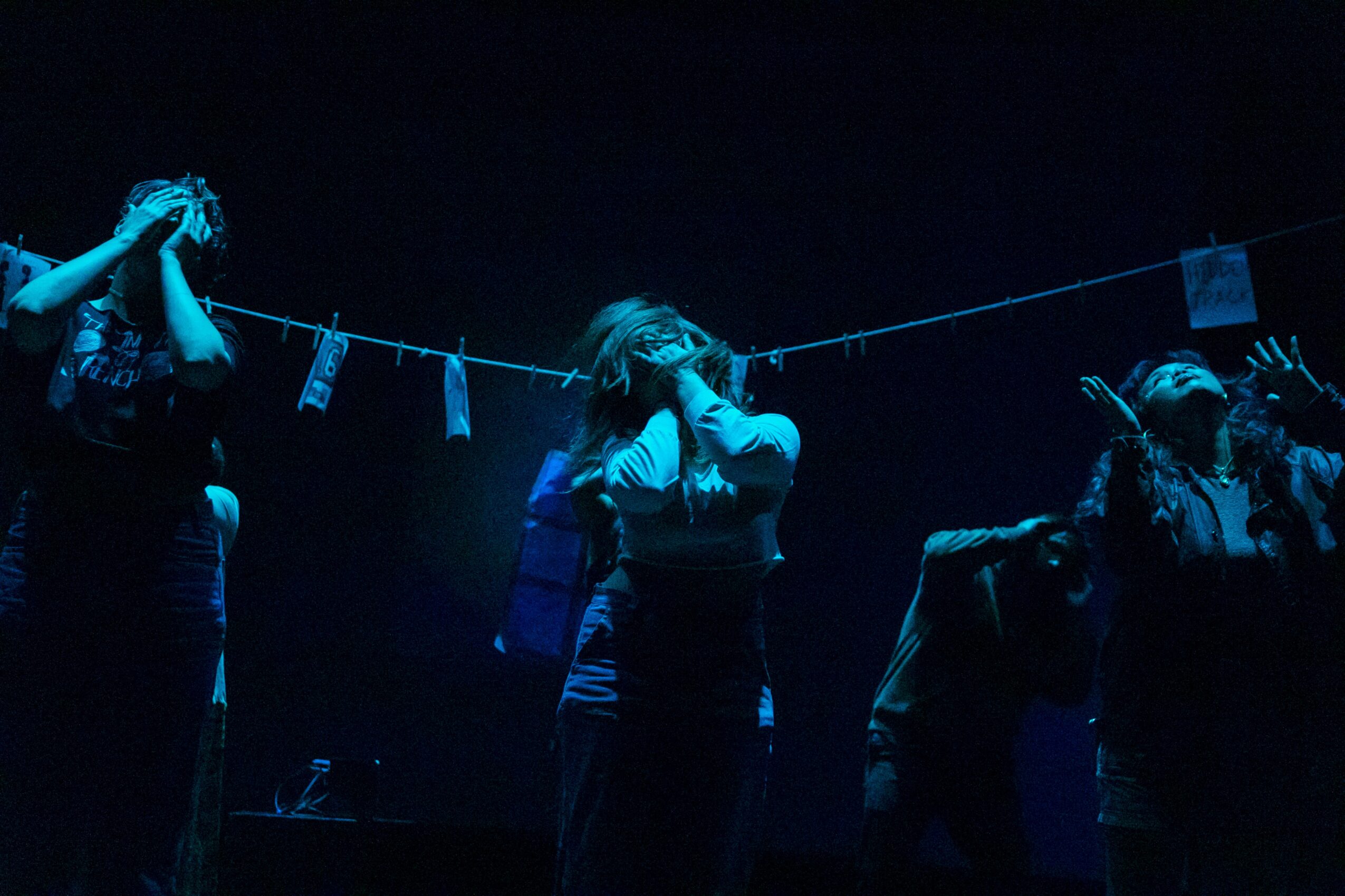 Group of people on stage with a dark background, some holding microphones, in a performance or event setting.