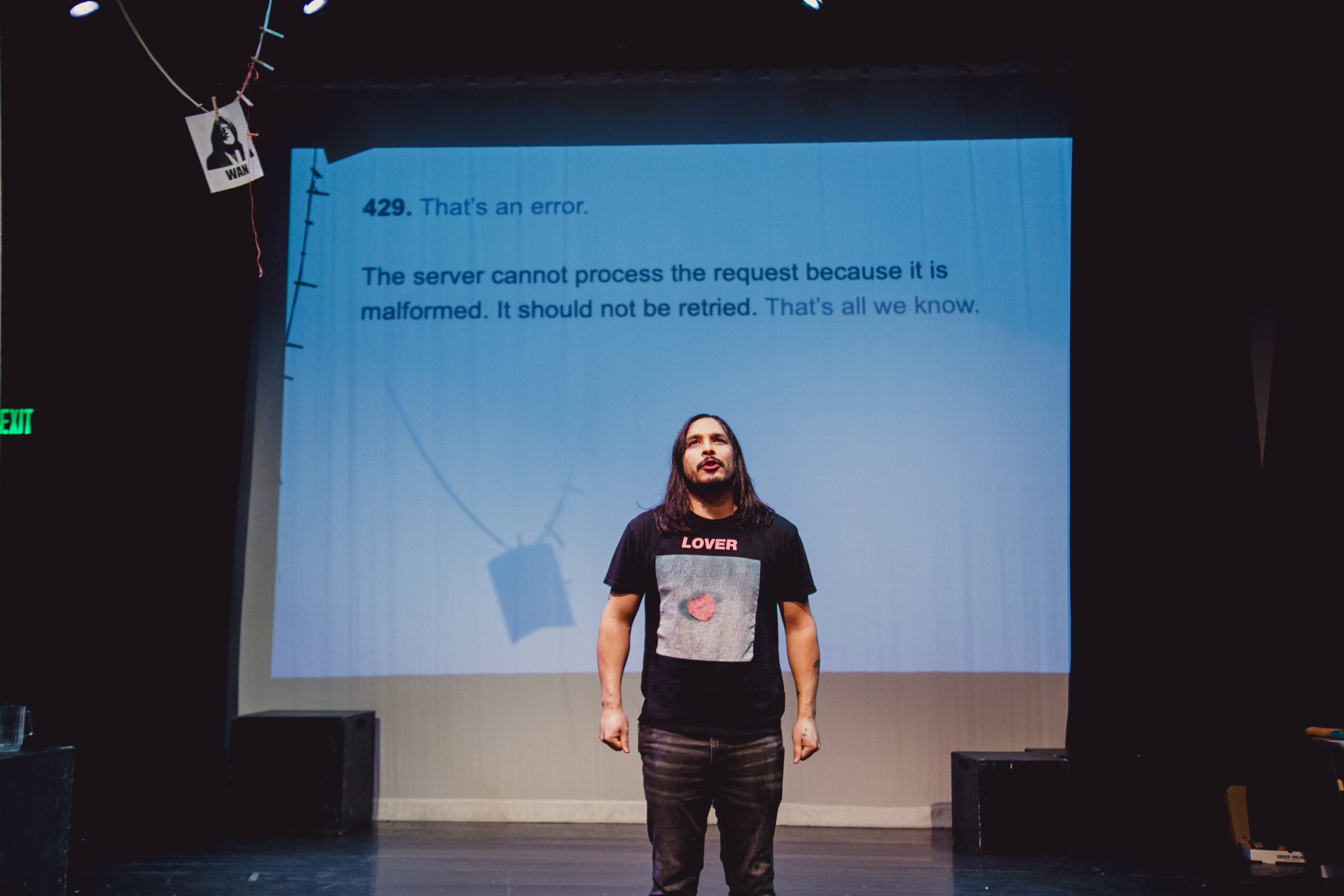 Person standing on stage in front of a large screen displaying an error message, with a dark background.