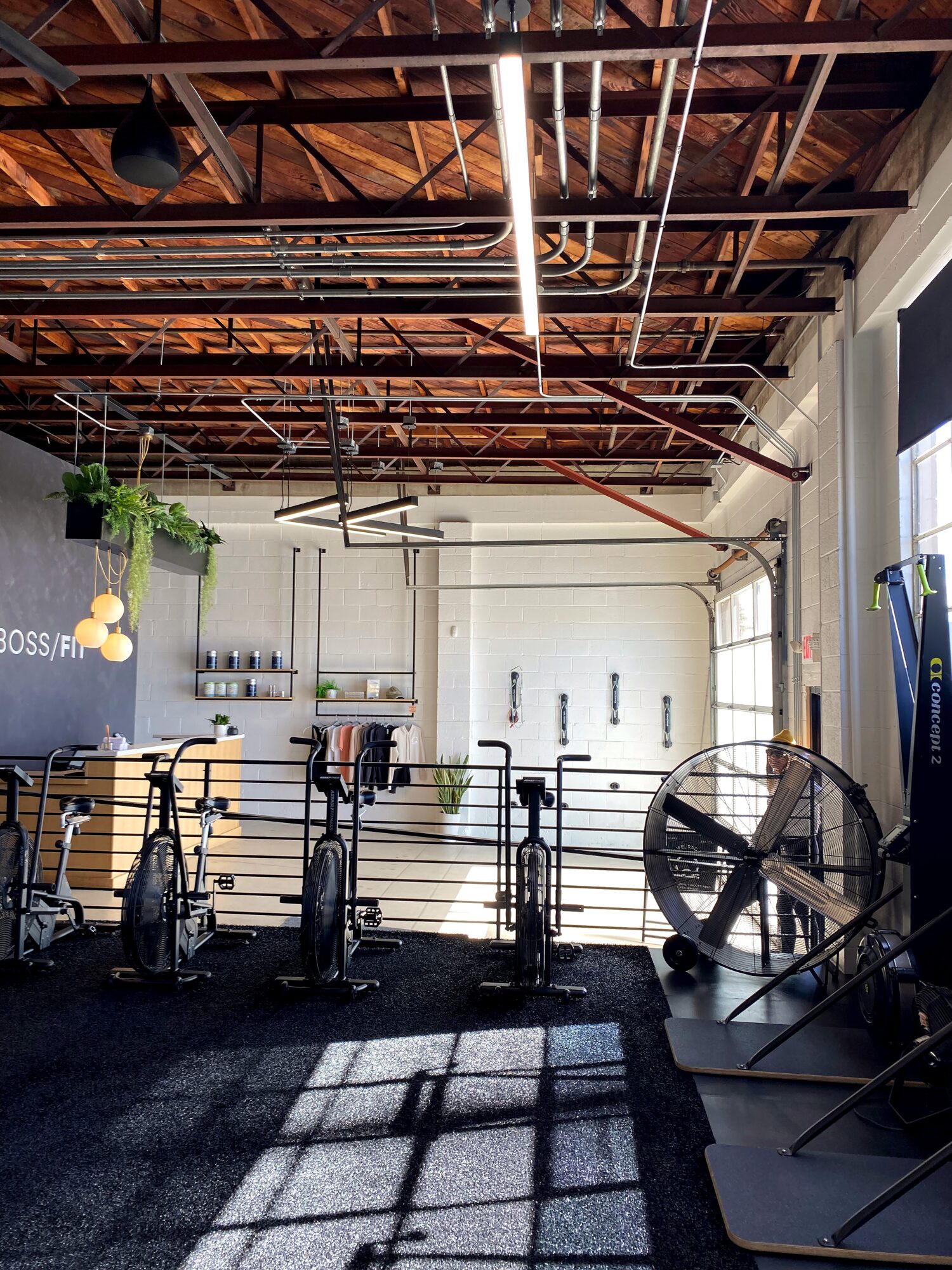 Gym with exercise bikes, large fan, and high ceiling with exposed wooden beams and pipes.