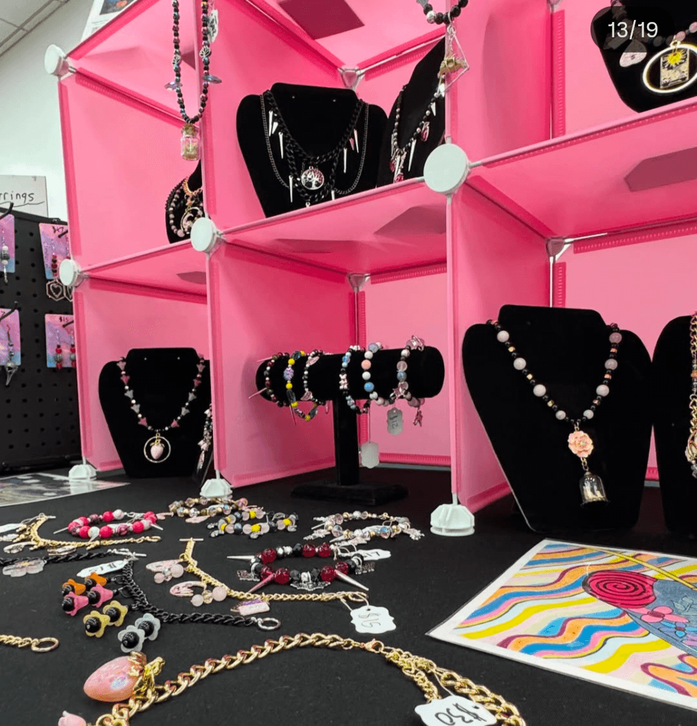 Display of necklaces, bracelets, and jewelry on pink shelves and black stands, with colorful jewelry and a patterned paper nearby.