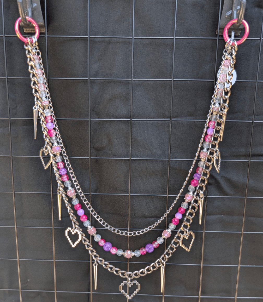Multi-layered necklace with pink beads, silver chains, and heart-shaped charms hanging, displayed on a black background.
