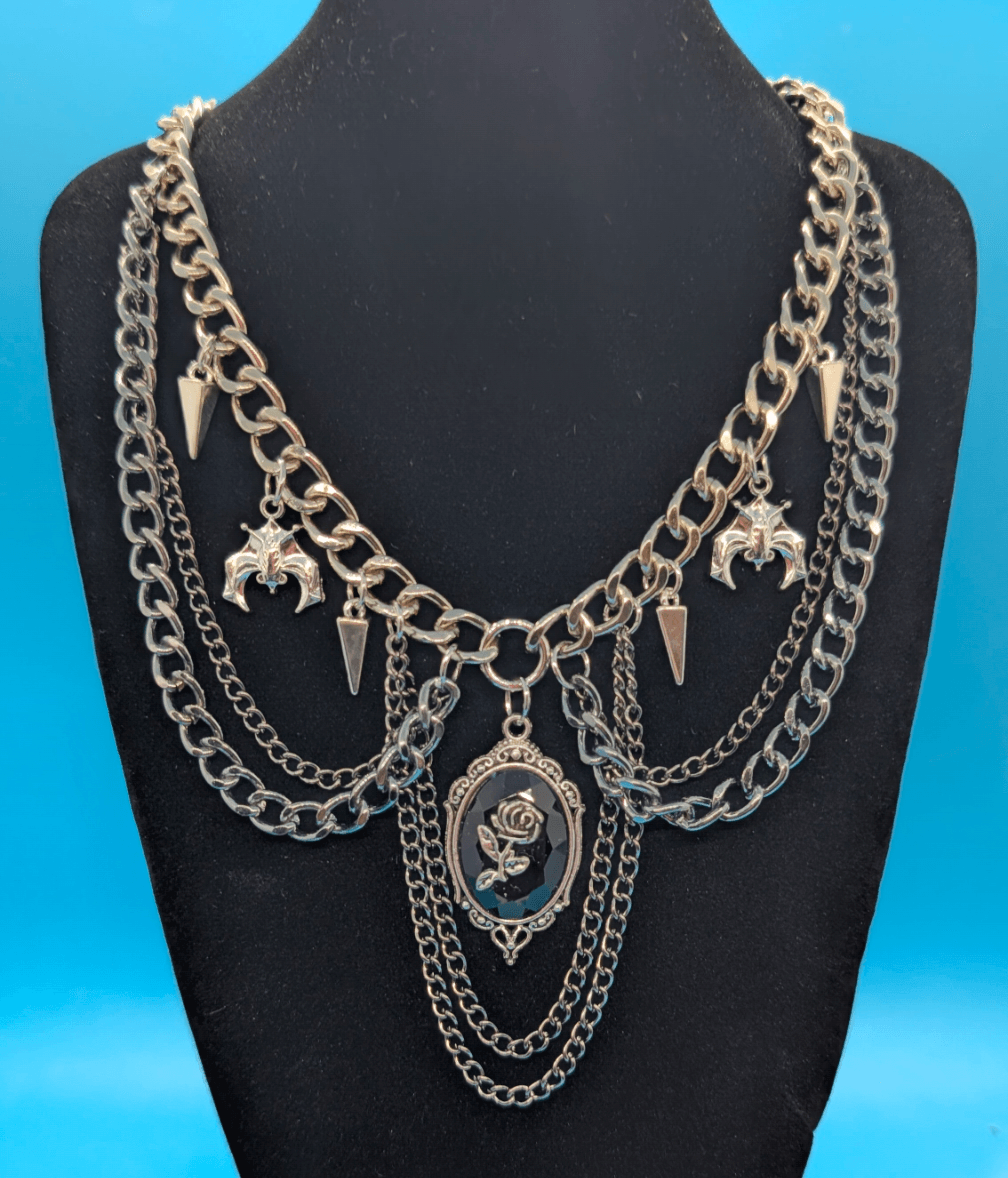 Silver layered chain necklace with charms and pendants displayed on a black bust against a blue background.