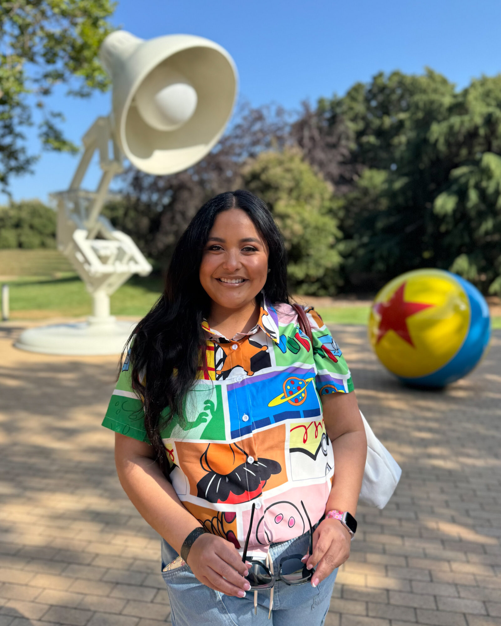 Smiling woman standing outdoors with trees and a large colorful ball in the background.