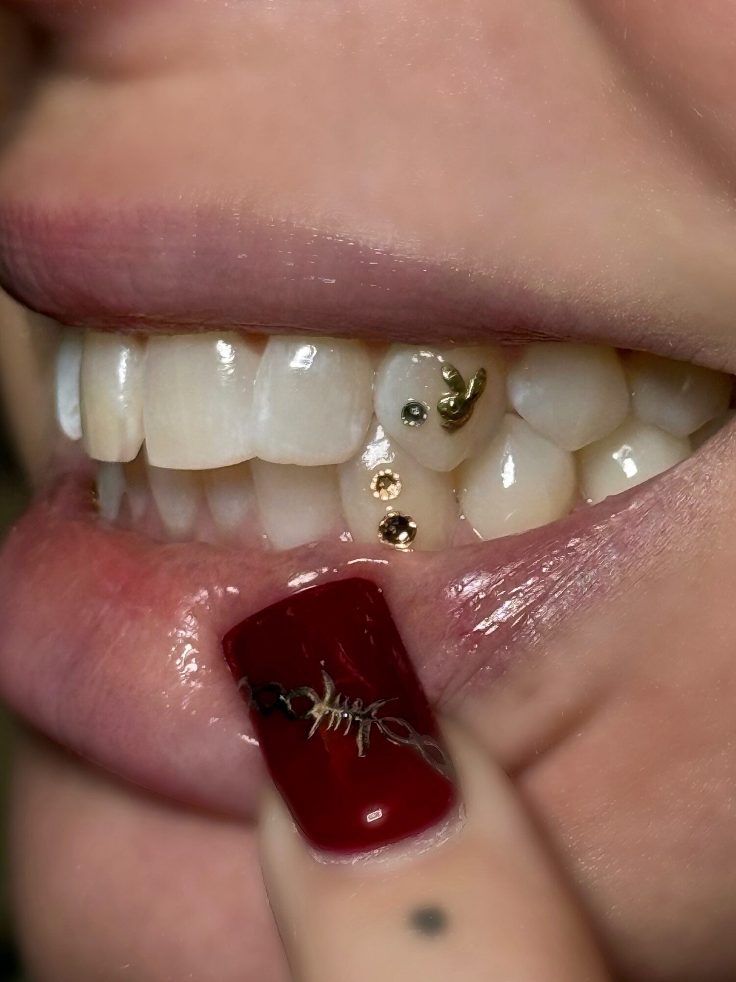 Close-up of a person's mouth showing teeth, lip piercings, and a finger with red nail polish touching the lip.