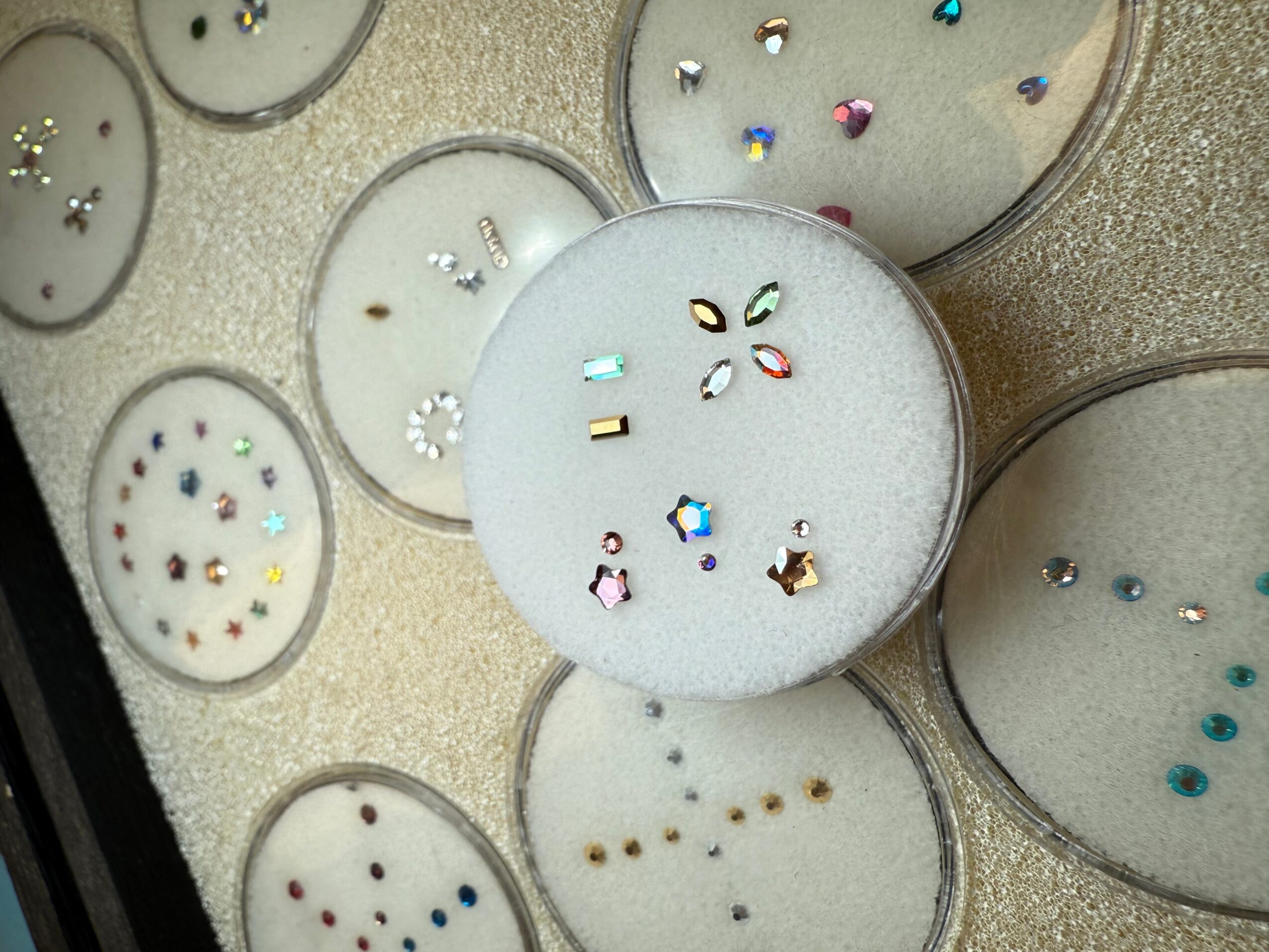 Small containers with colorful rhinestones or beads on white foam, arranged in a pattern.