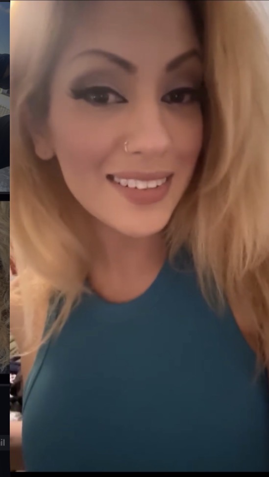 Close-up of a smiling woman with makeup and a nose piercing, wearing a teal top.