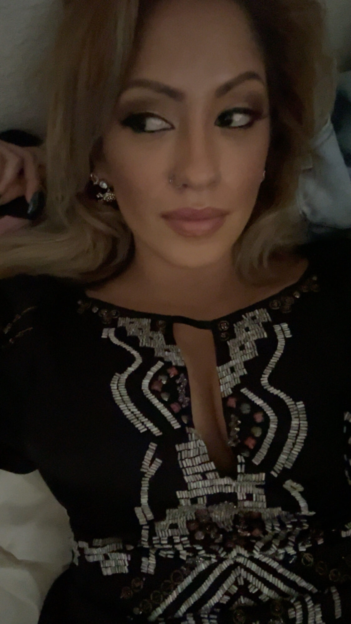 Woman with light brown hair lying down, wearing a black top with intricate white and silver embroidery.