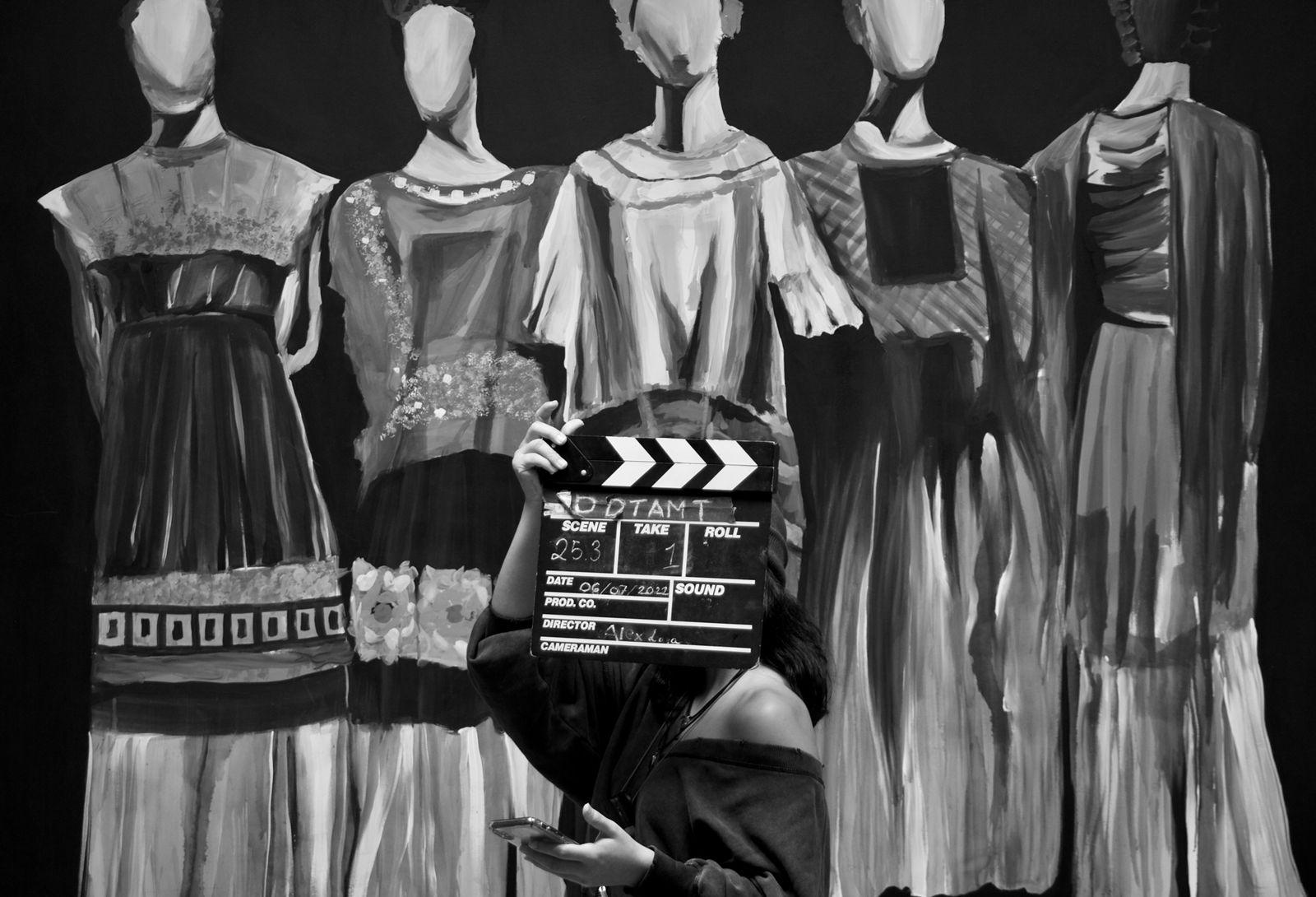 Person holding a clapperboard in front of a display of mannequins dressed in vintage clothing.