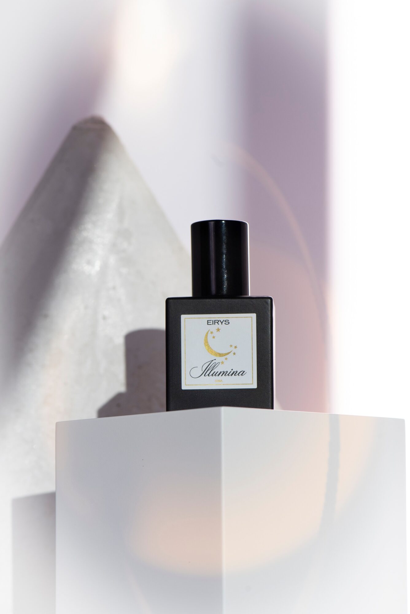 Black perfume bottle with a white label on a white surface, shadow cast to the left, background with soft light and shadows.