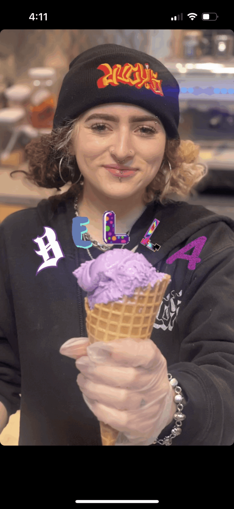 Person wearing a black beanie holding a purple ice cream cone with colorful candles, smiling outdoors.