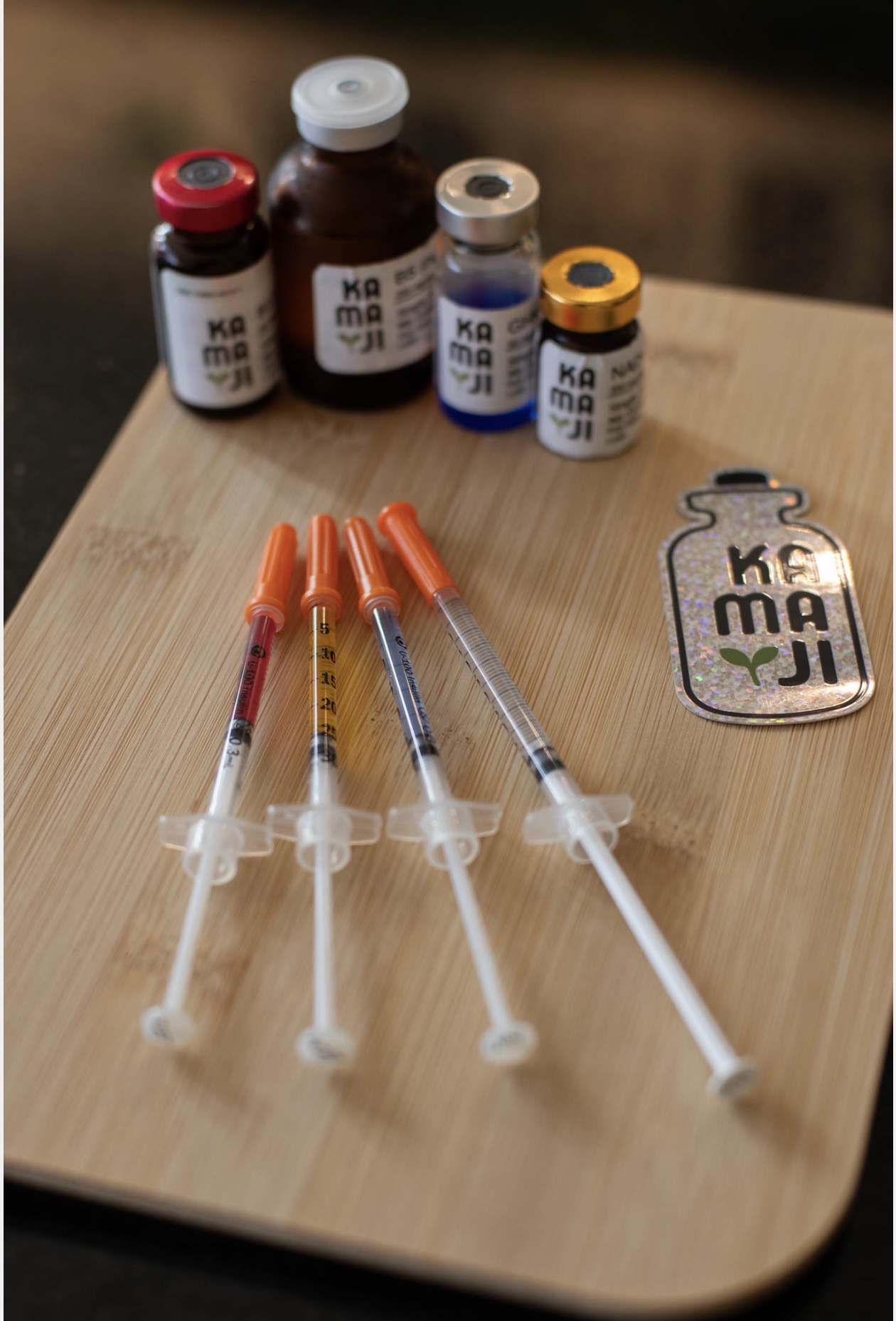 Four syringes with orange caps and four small bottles of medication on a wooden surface, with a keychain-shaped object nearby.