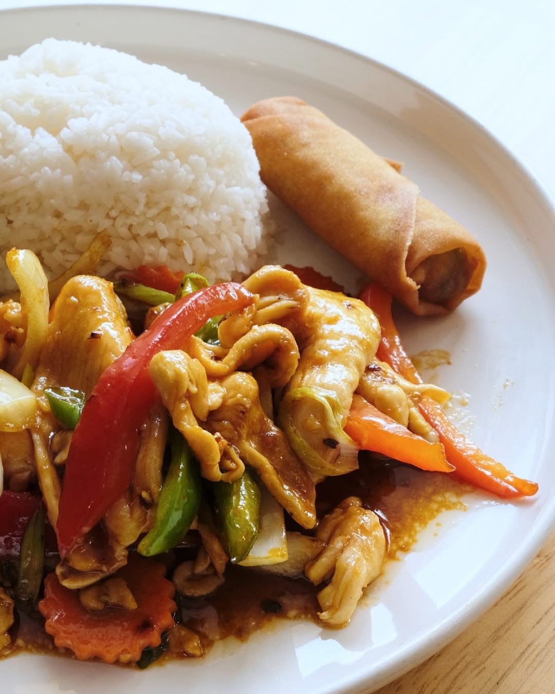 Plate with rice, spring roll, and stir-fried vegetables with chicken, red bell pepper, and carrots.