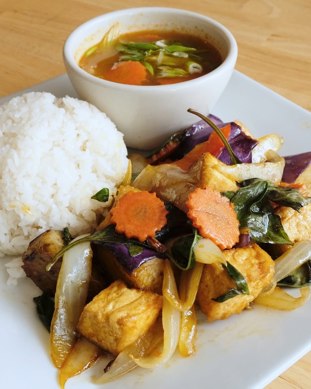 Plate with rice, vegetable stir-fry, and a bowl of soup on a wooden table.