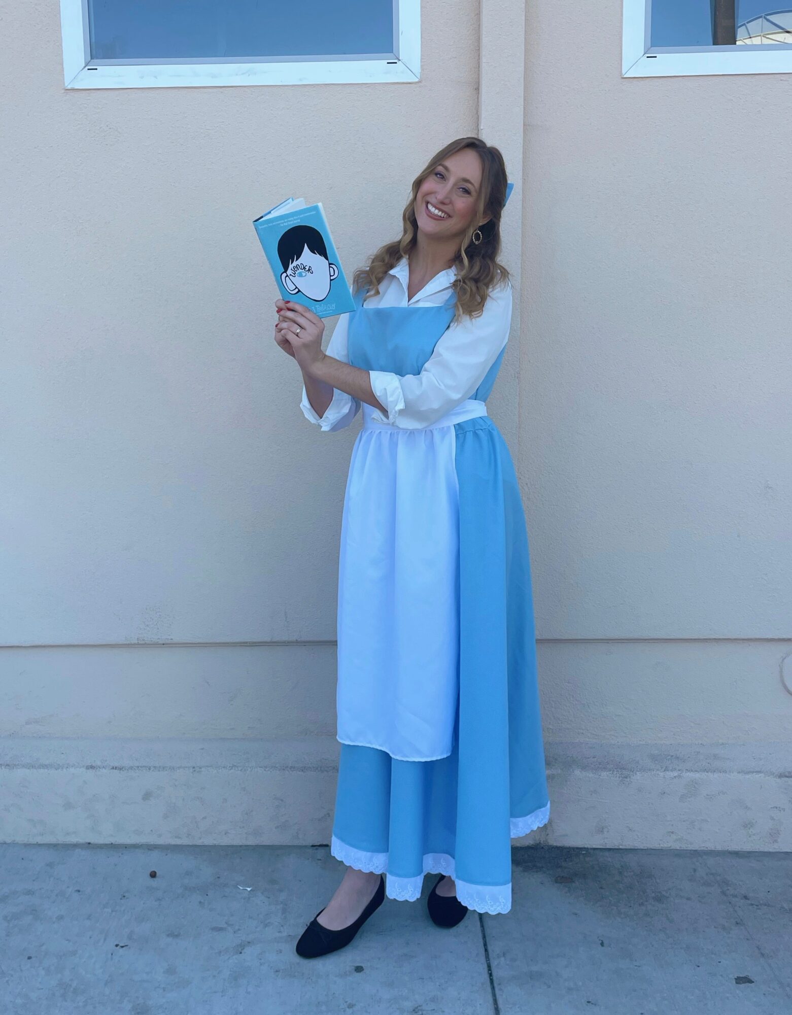 Woman in a blue and white dress holding a sign with a penguin, standing outdoors against a beige wall.