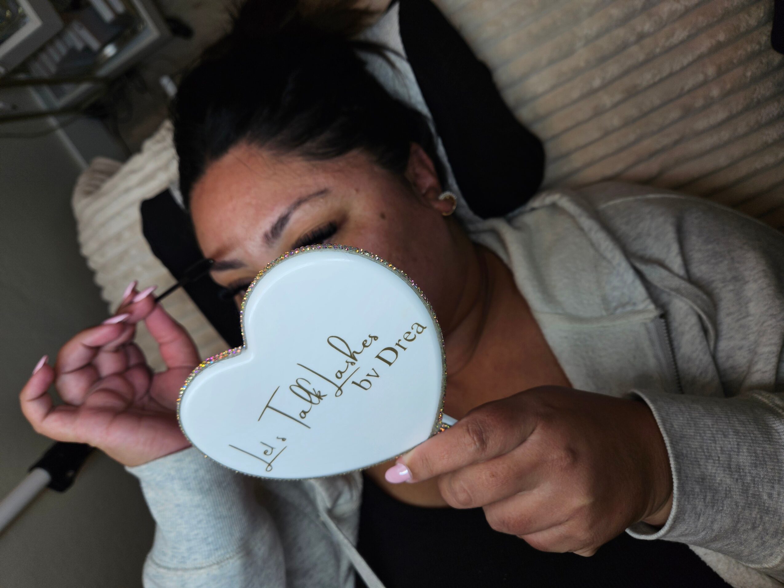 Person lying on a couch holding a heart-shaped mirror with handwritten text, partially covering their face.