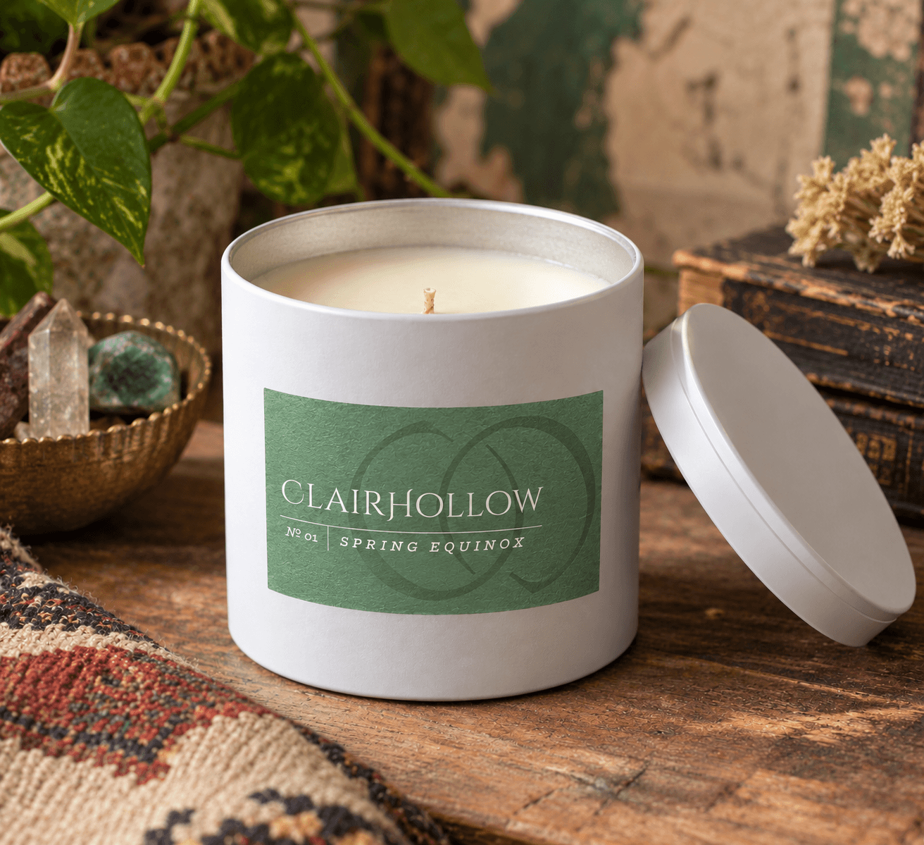 White candle in a container with a green label reading 'Clairhollow' and 'Spring Equinox' on a wooden surface.