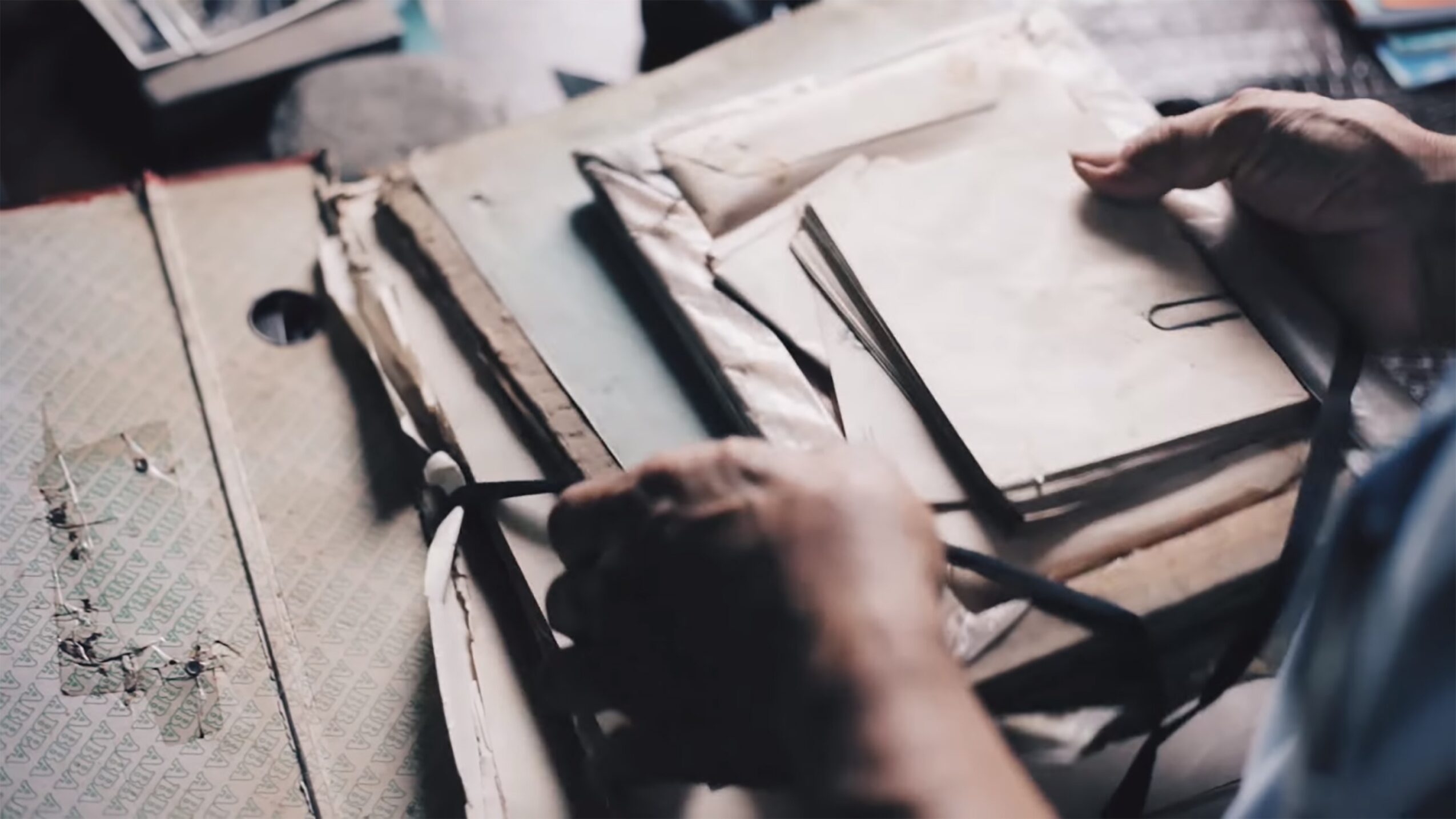 Person's hands handling old, worn books and papers on a cluttered surface.
