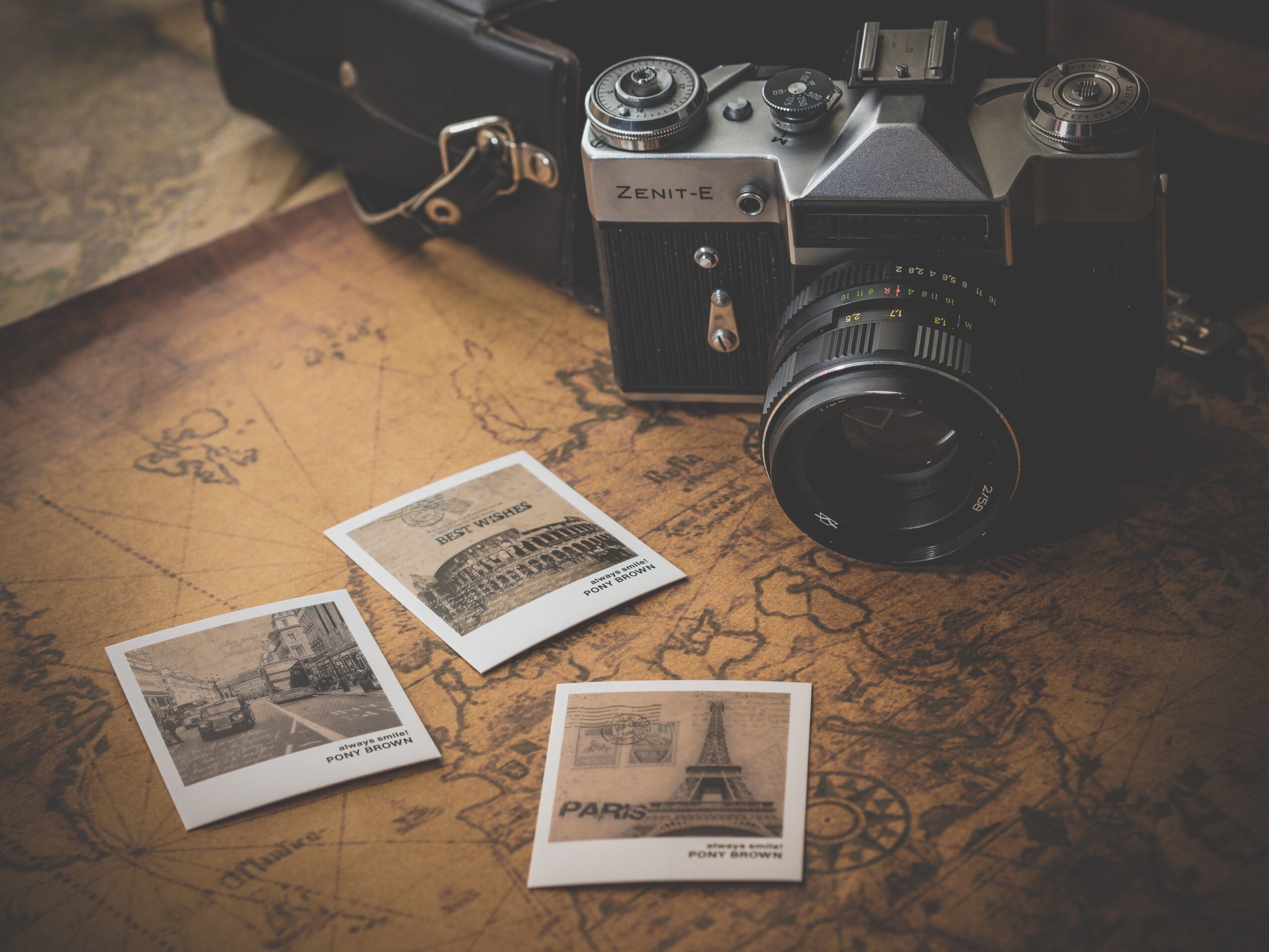 Camera with three photographs on a wooden surface, one showing the Eiffel Tower, another a cityscape, and the third a building.