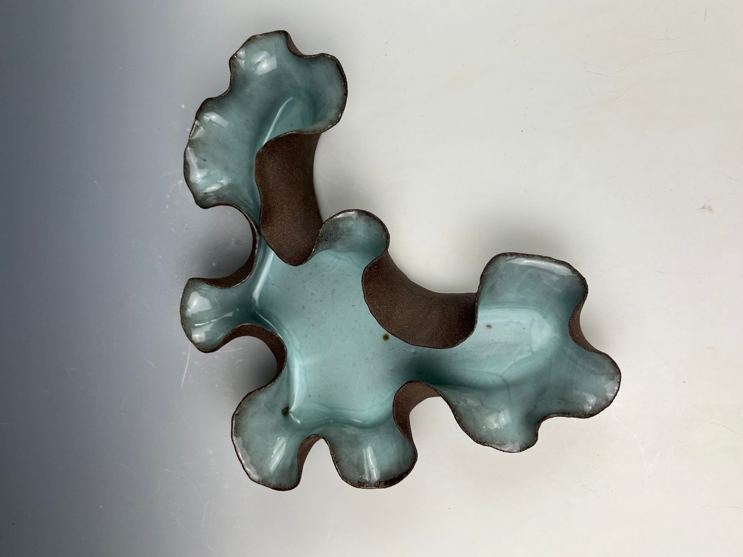 A glass sculpture with irregular, rounded shapes and a mix of transparent and opaque sections, mounted on a white wall.