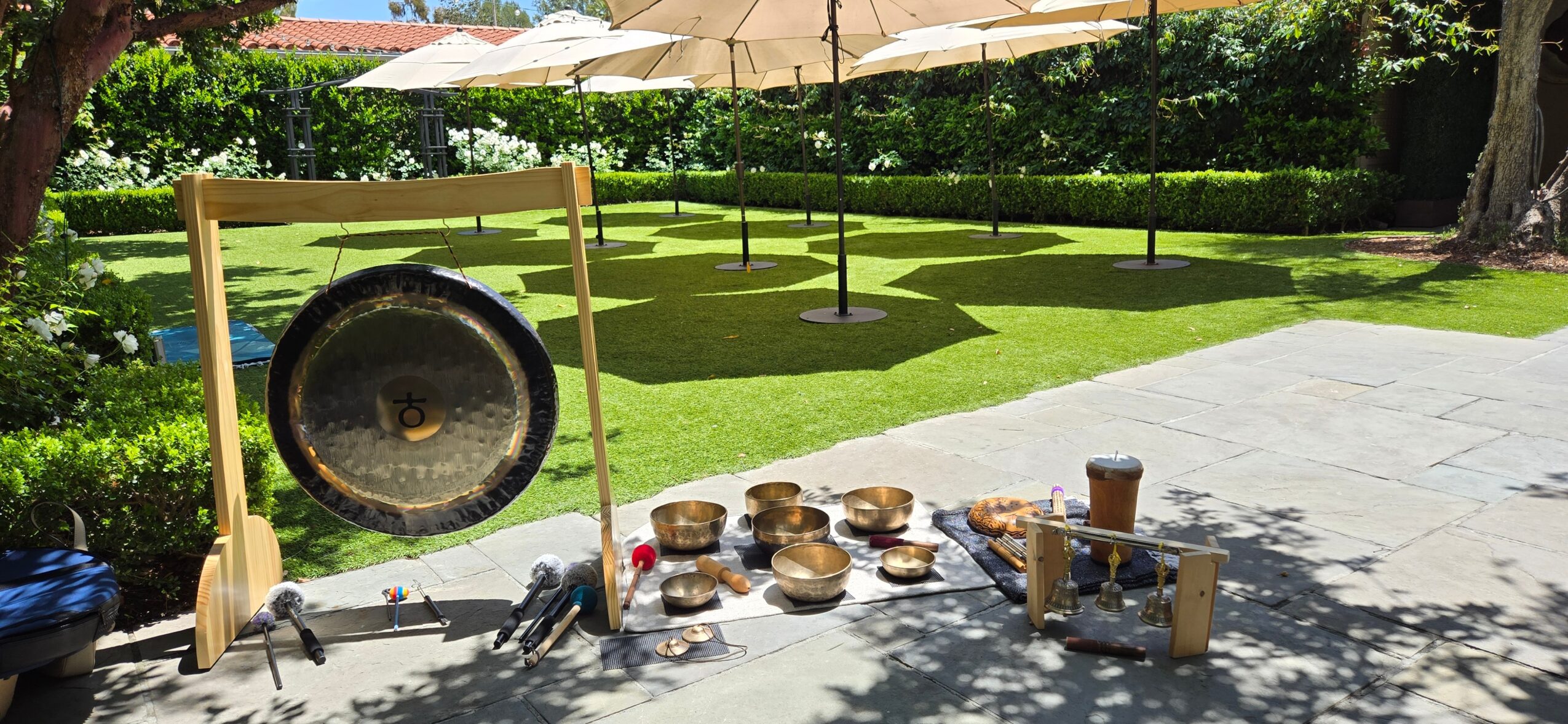 Gong and musical instruments on a paved outdoor area with umbrellas and greenery in the background.