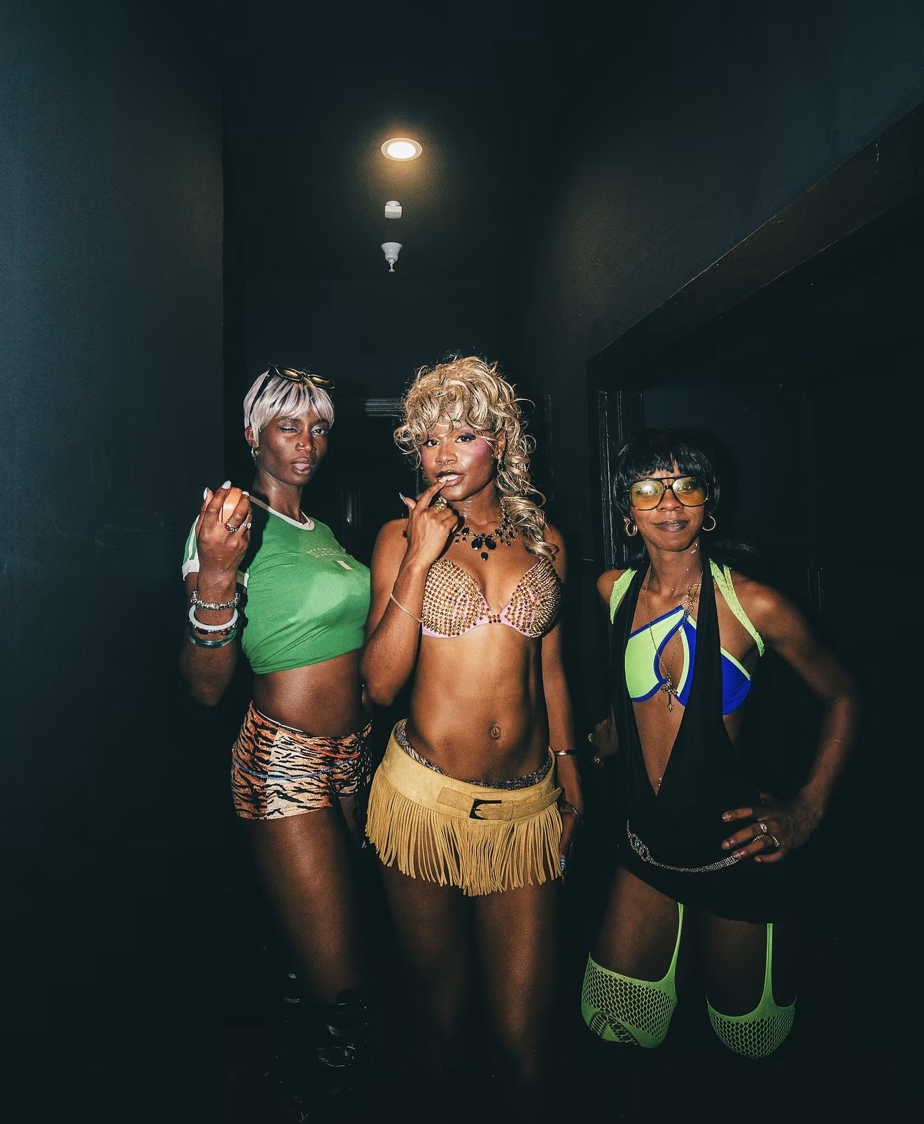 Three people pose in a dim hallway wearing colorful performance outfits.